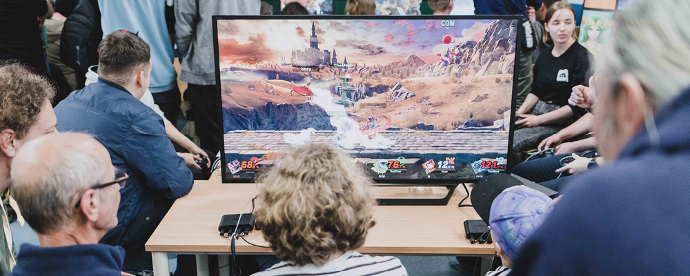Mehrere Besucher der Computerspielenacht sitzen vor einem PC und verfolgen ein sehr aufwendig gestaltetes Spiel.